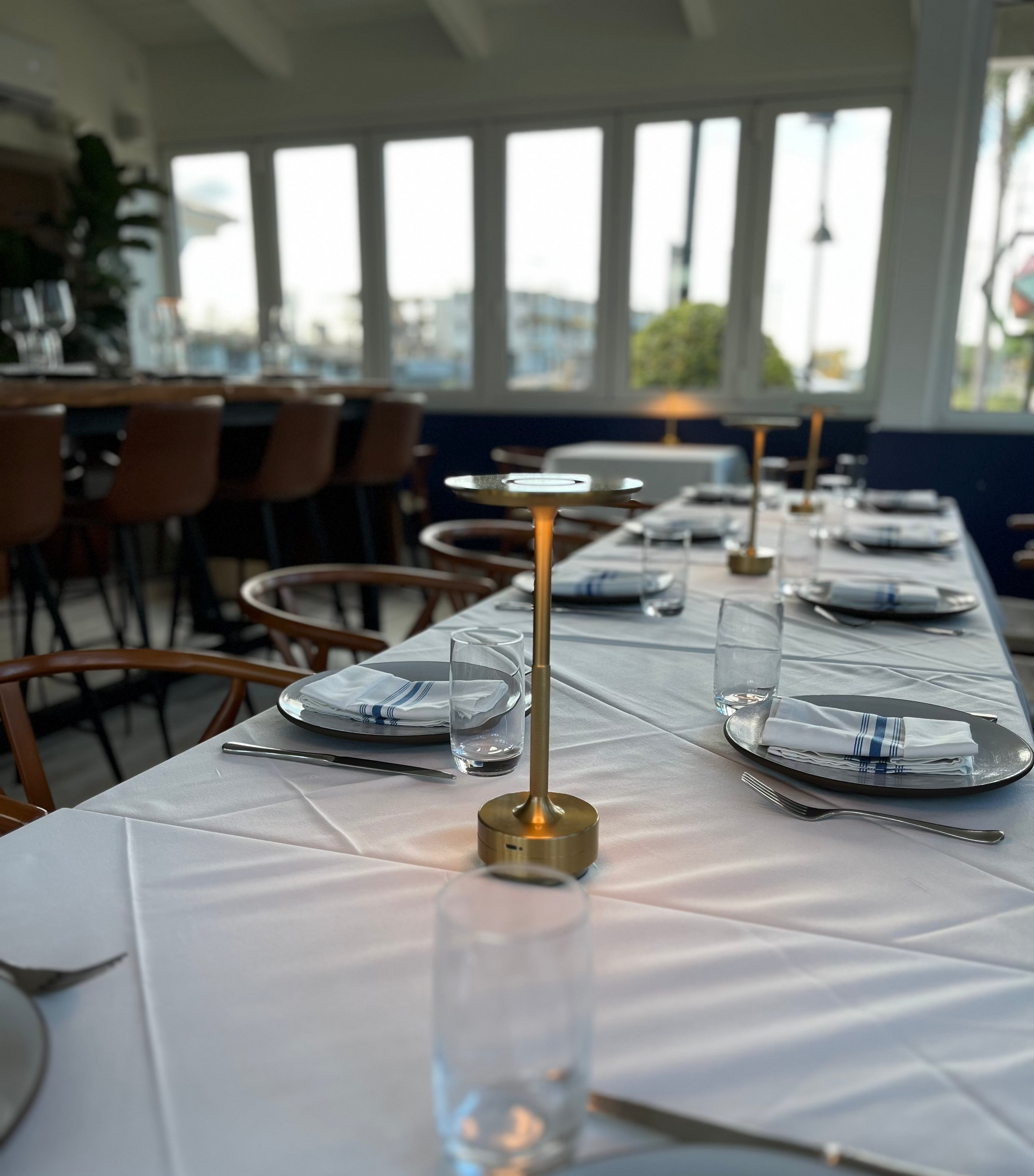 Dining table set with plates, glasses, and a central light in Nicholson Muir Fine Dining Restaurant in Boynton Beach.