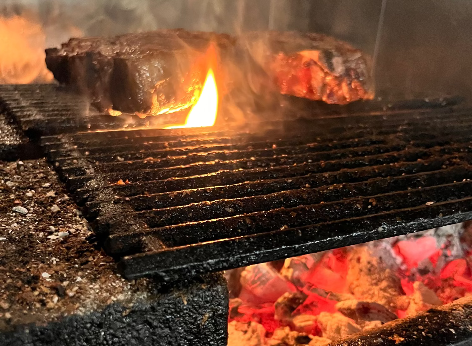 Close-up of a lit grill with glowing quebracho and charcoals and flames. Nicholson Muir Fine Dining cooking meats wagyu prime filet ribeye